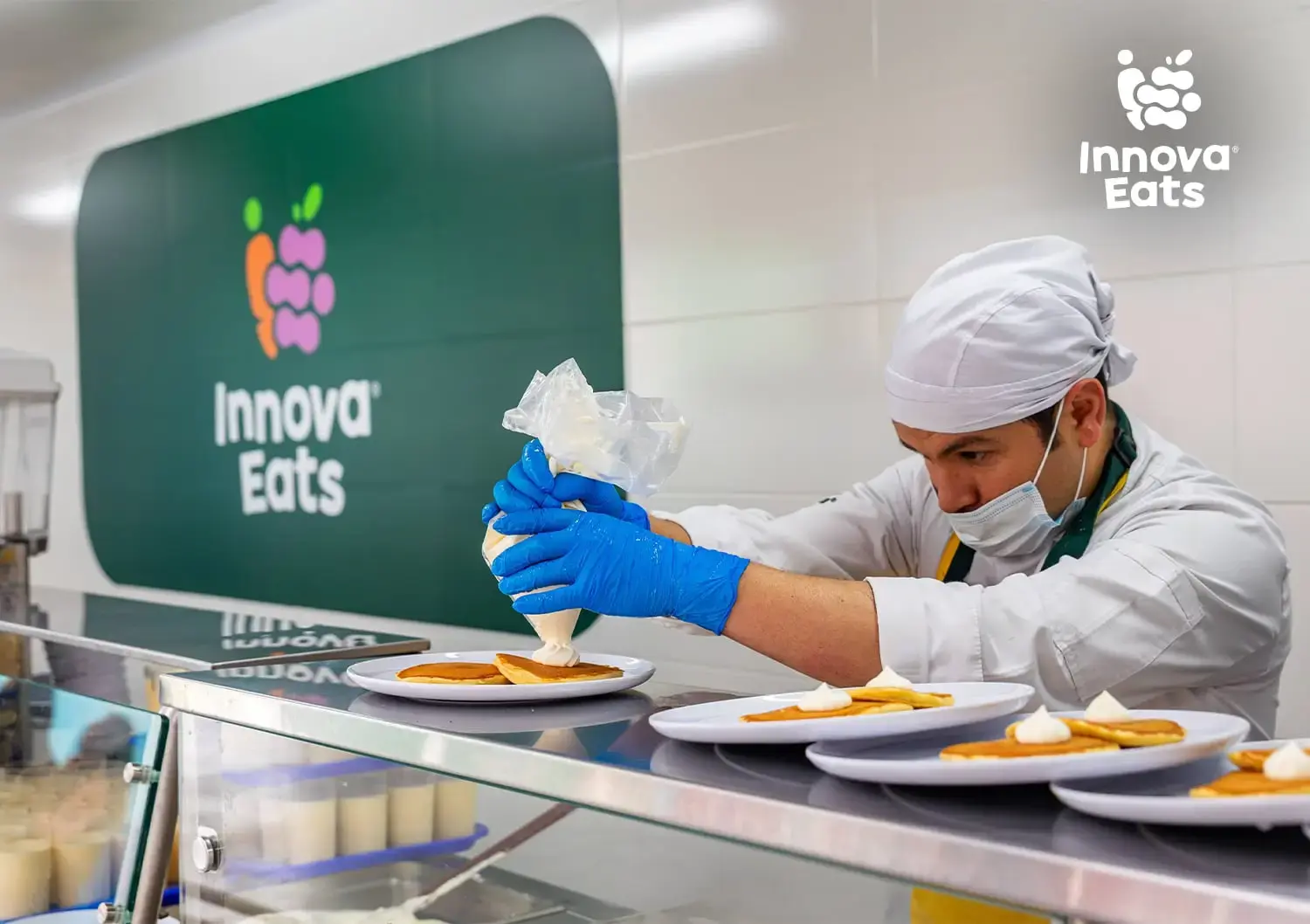 Cocinero profesional con uniforme blanco y gorro preparando bandejas de comida saludable en la cocina de Innova Eats.