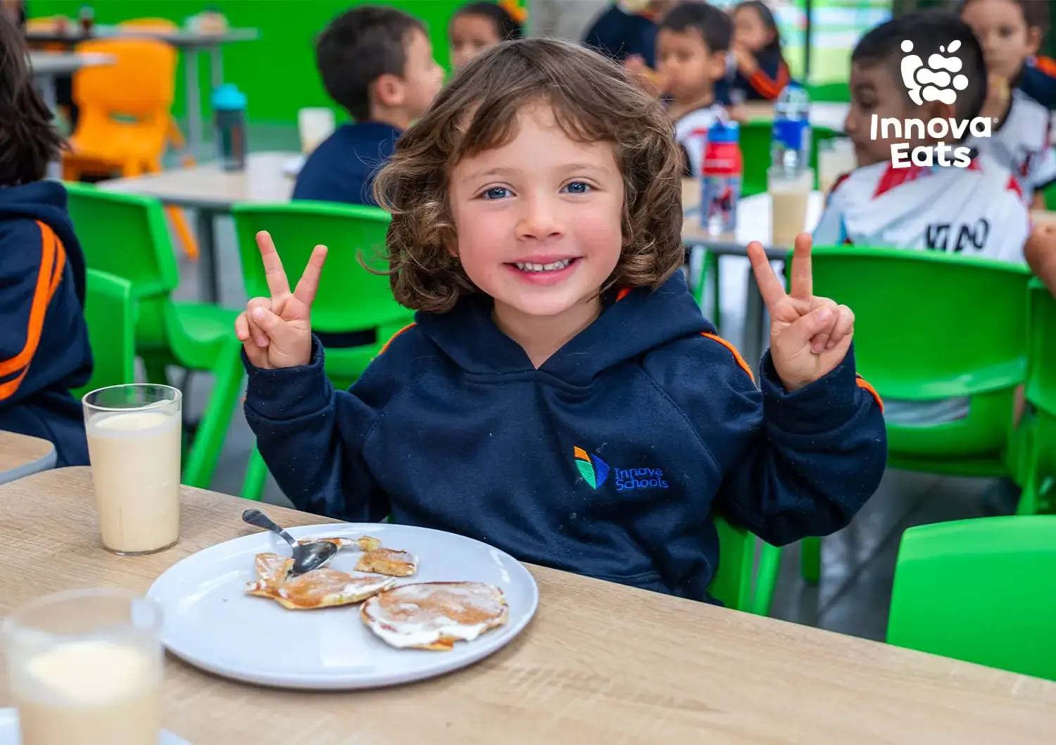 Niño almorzando felizmente junto a sus compañeros en las mesas del comedor estudiantil de Innova Eats.