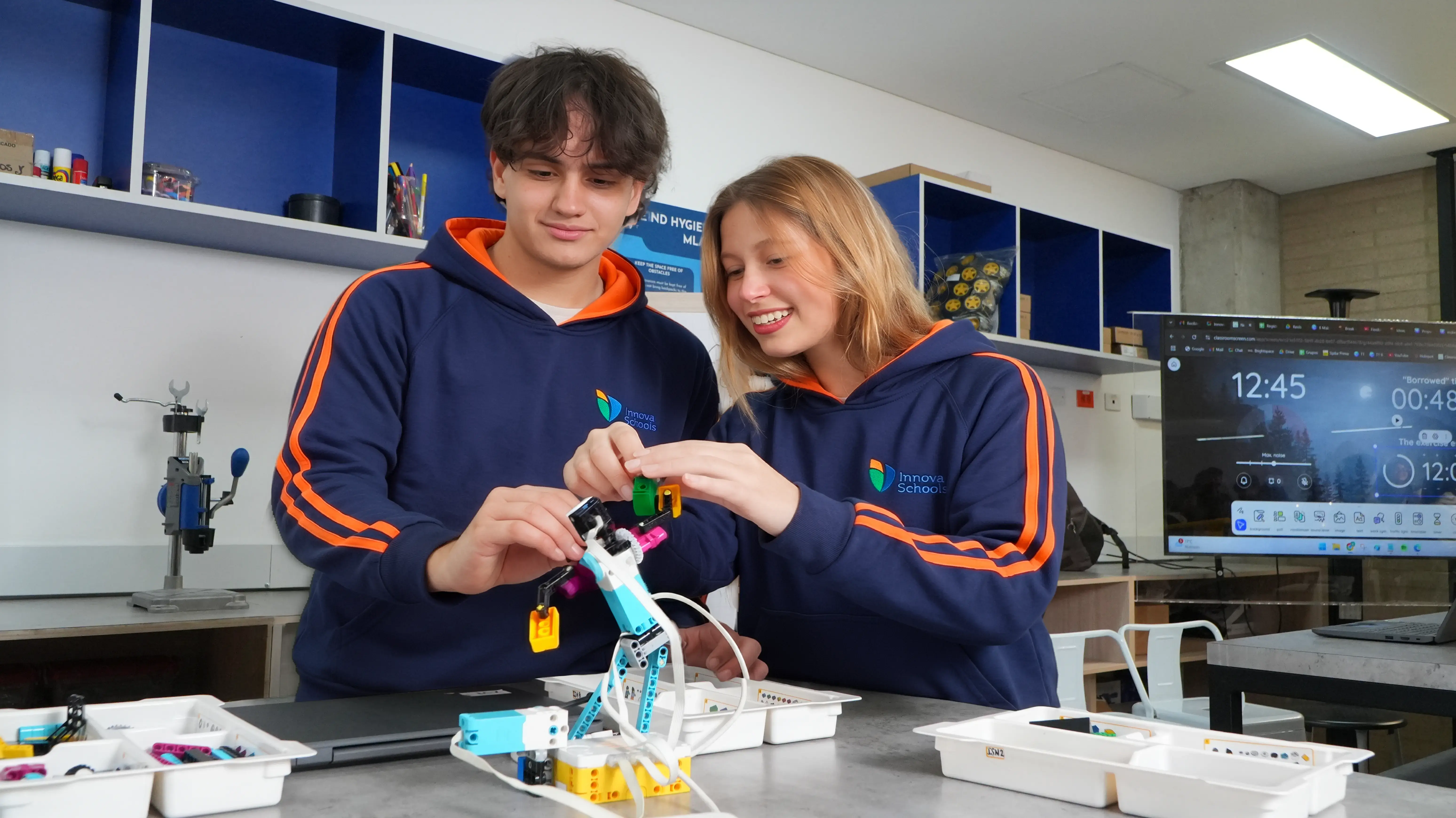 Dos estudiantes de bachillerato con uniforme de Innova Schools sonríen mientras ensamblan juntos un proyecto de robótica y tecnología STEM en el laboratorio del colegio.