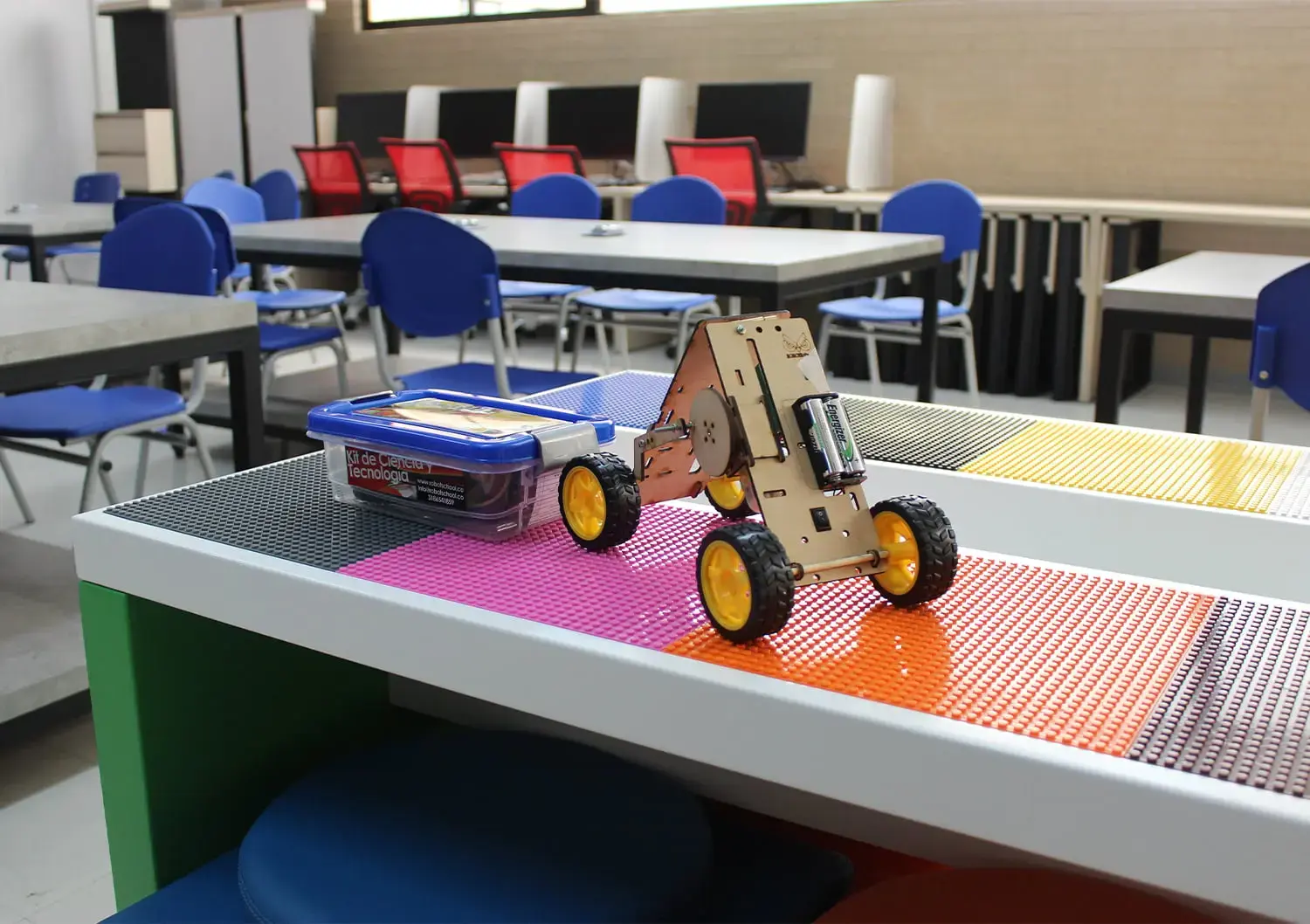 Prototipo de coche robótico de madera con ruedas amarillas sobre una mesa temática en un aula STEM.