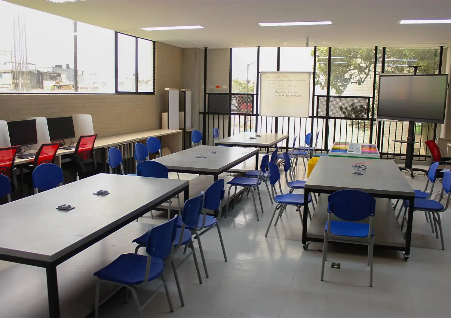 Aula de robótica y tecnología equipada con mesas de trabajo compartidas, sillas azules y pantallas digitales.