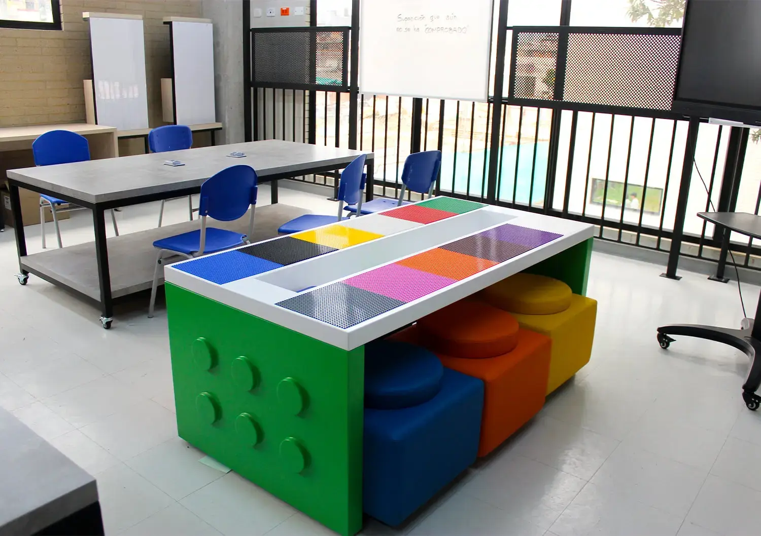 Mesa de bloques de construcción de colores con taburetes modulares en un taller de robótica escolar.